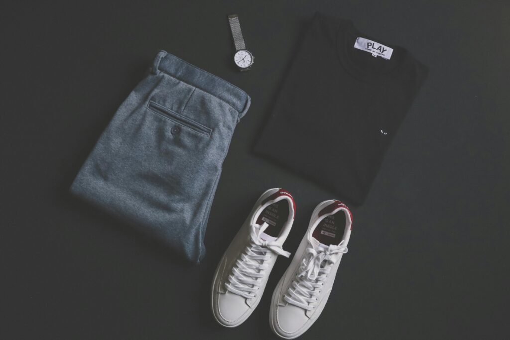 A stylish flat lay featuring jeans, t-shirt, sneakers, and a wristwatch on a dark background.